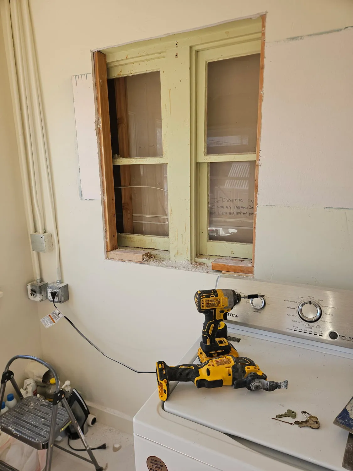 An old wood double-hung window exposed to the studs, with handwriting on the glass reading Joe Denter, I Noah Guy Handyman Services, found it like this, left my mark