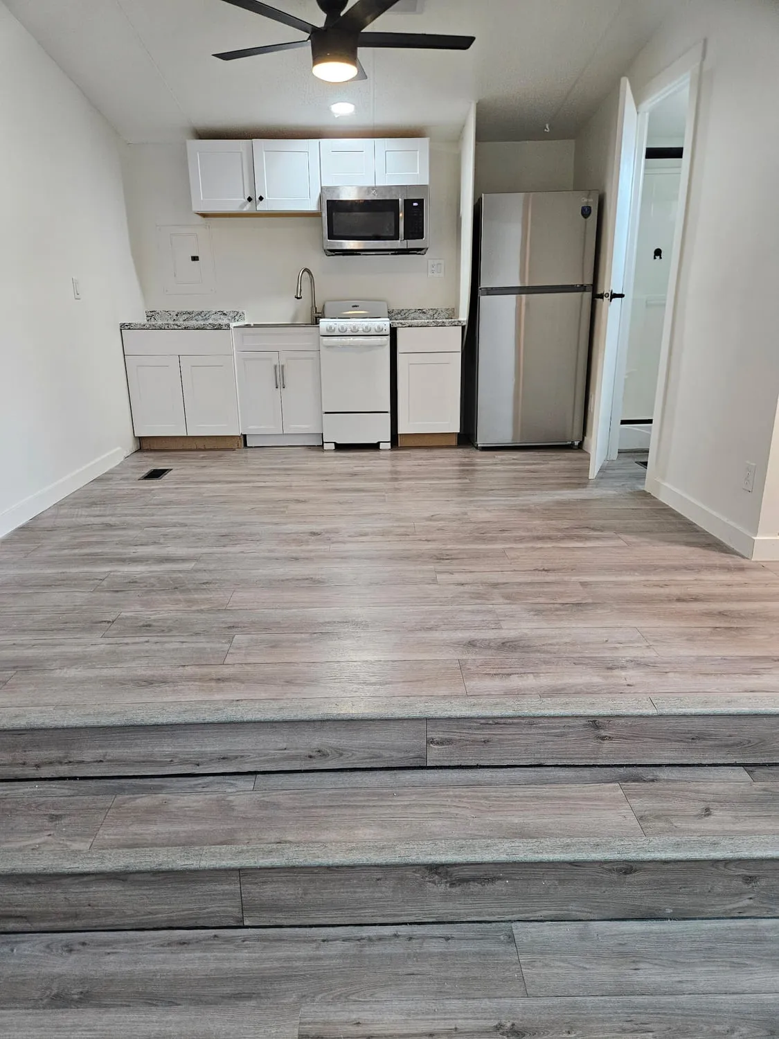 A finished studio unit with grey-oak laminate plank flooring, a white shaker kitchenette with granite counters and stainless appliances