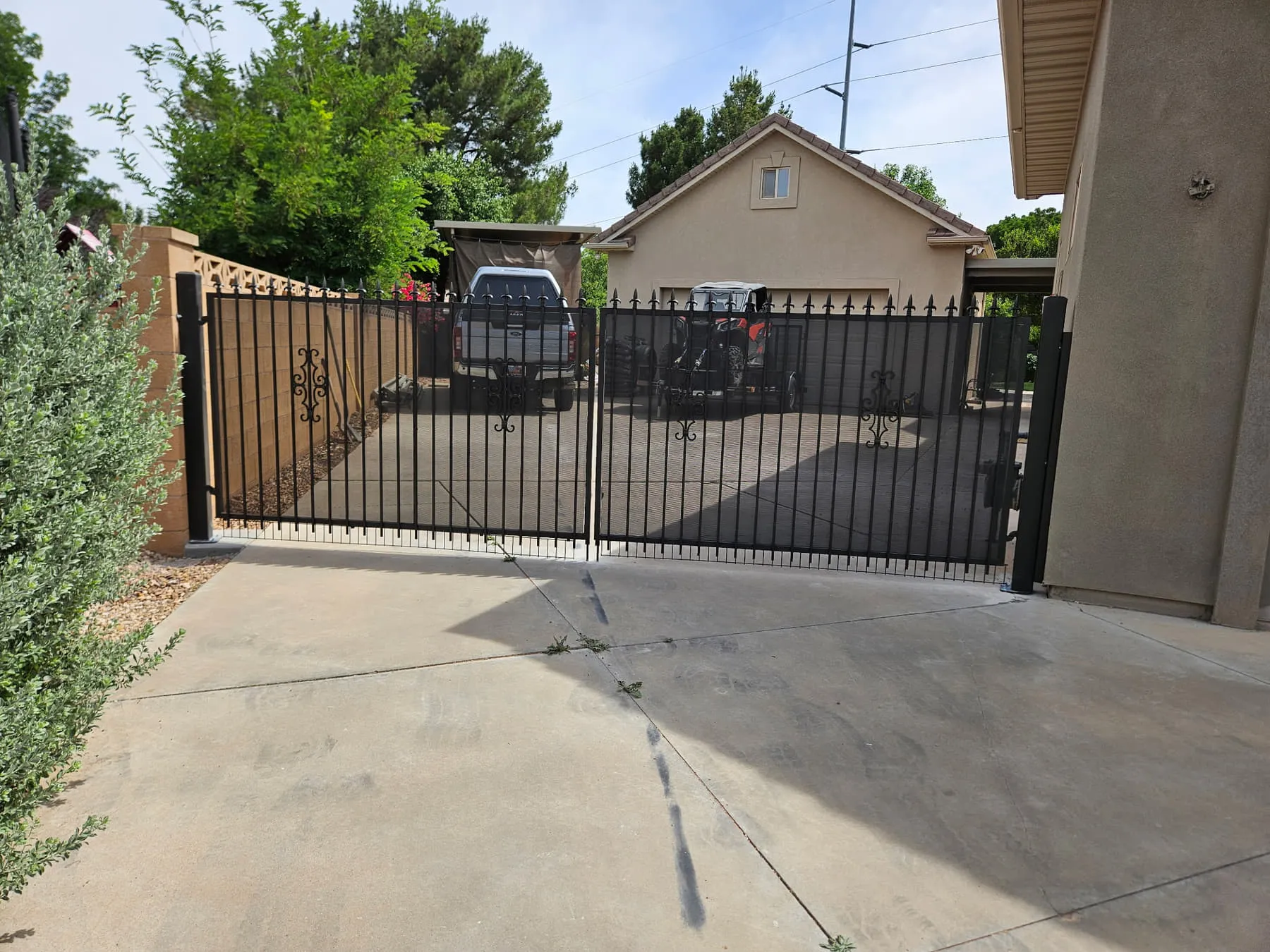 A new matte-black iron double driveway gate with a matching pedestrian gate on black posts across the same concrete driveway