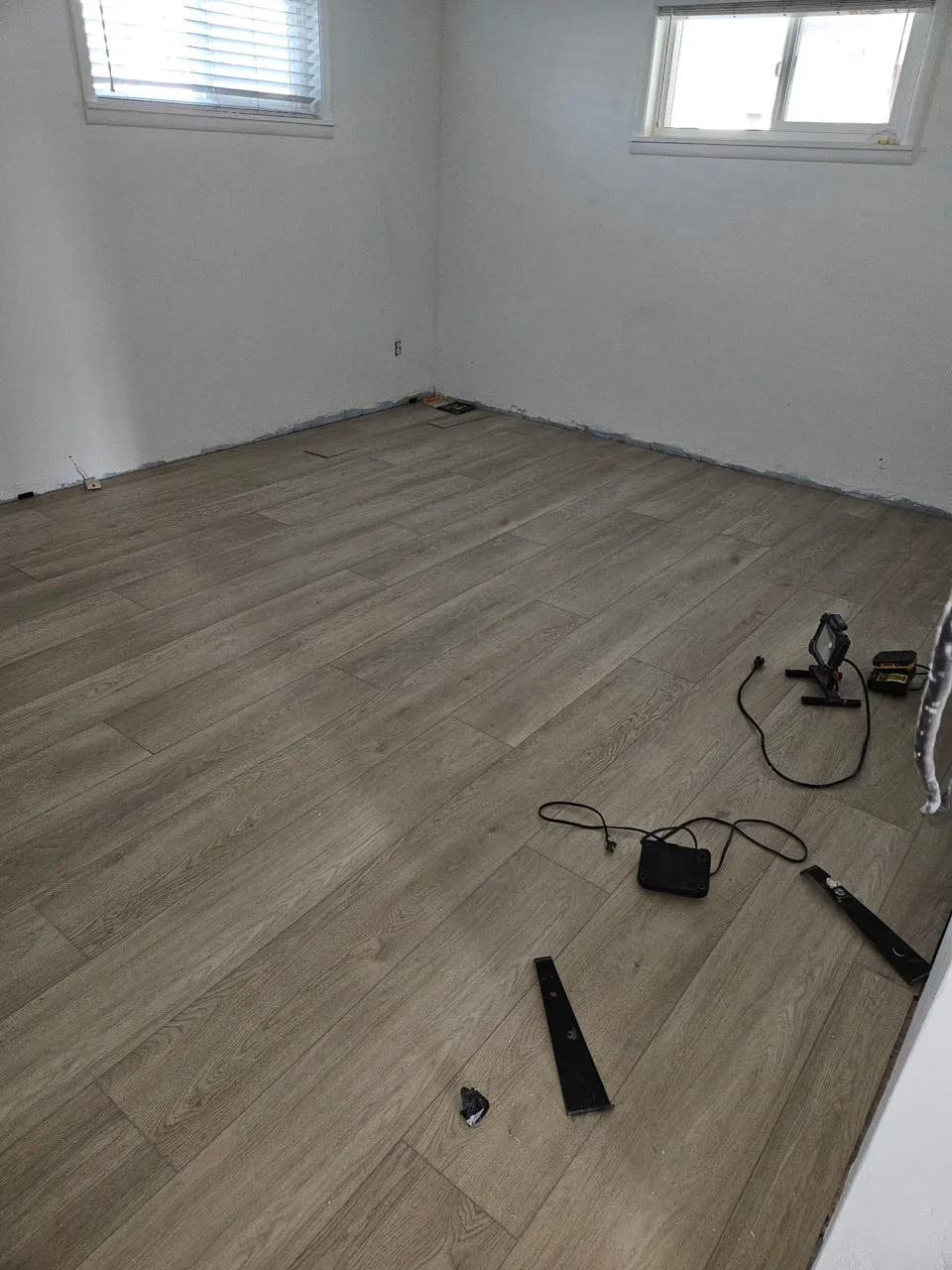 An empty bedroom with grey-oak laminate plank flooring complete, white walls and two small high windows
