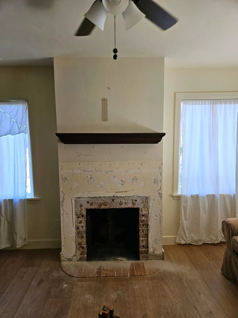 The same farmhouse fireplace with a new dark-stained mantel shelf installed while the plaster patches are still unpainted
