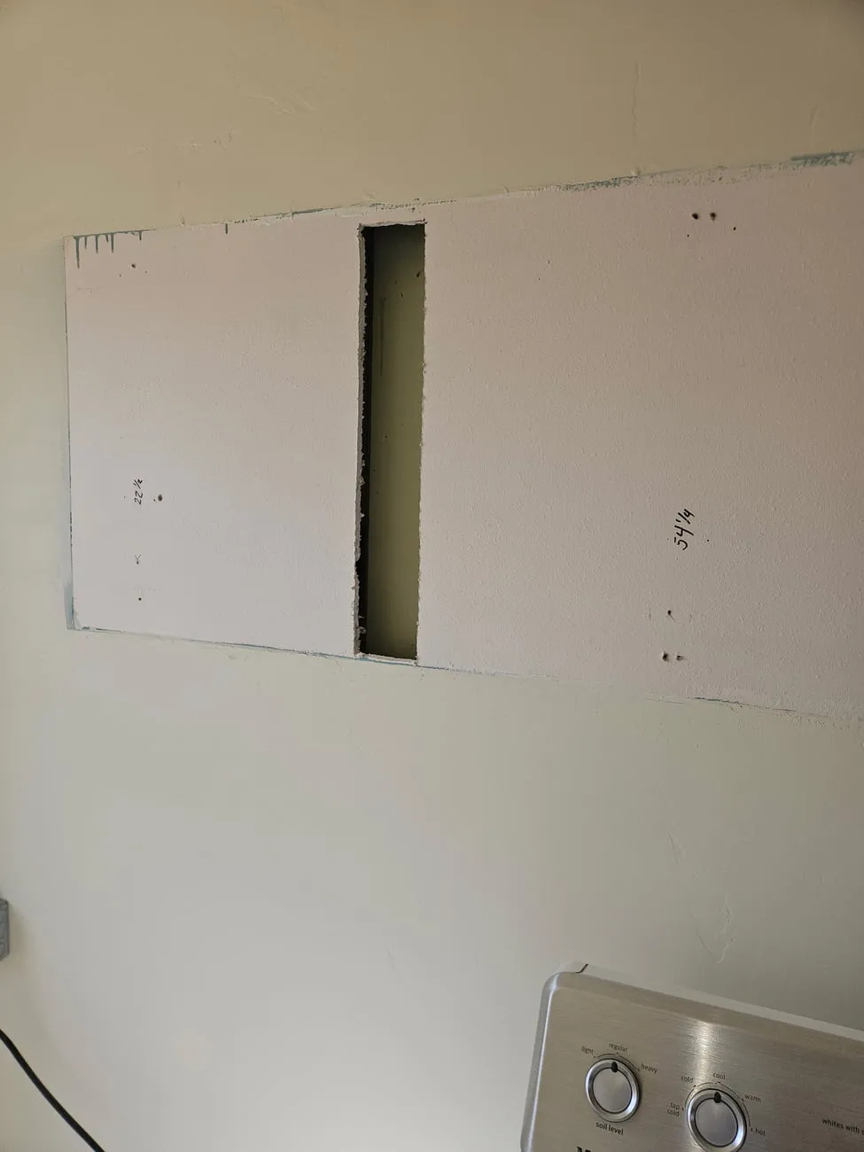 A large taped and first-coated drywall patch where a window opening was framed and closed, with pencilled dimensions written on it