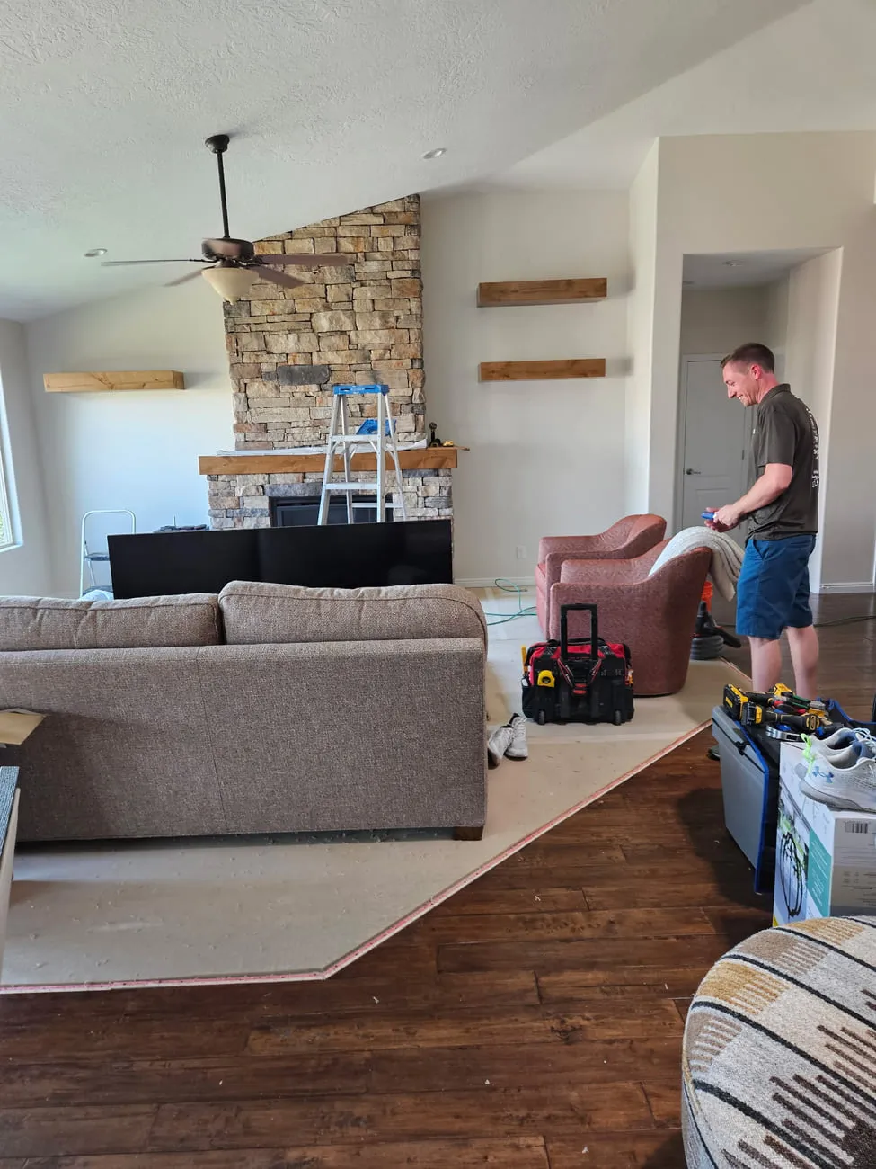 The same great room with three stained floating shelves mounted on the walls flanking the stacked stone fireplace