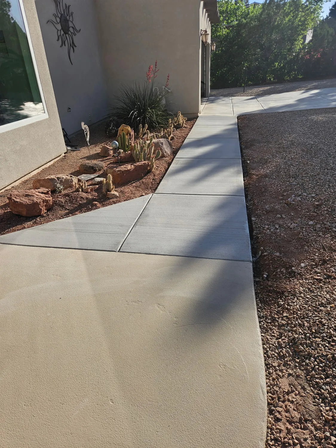 A wide finished concrete walkway with clean control joints, tooled edges and a radius corner beside a cactus bed