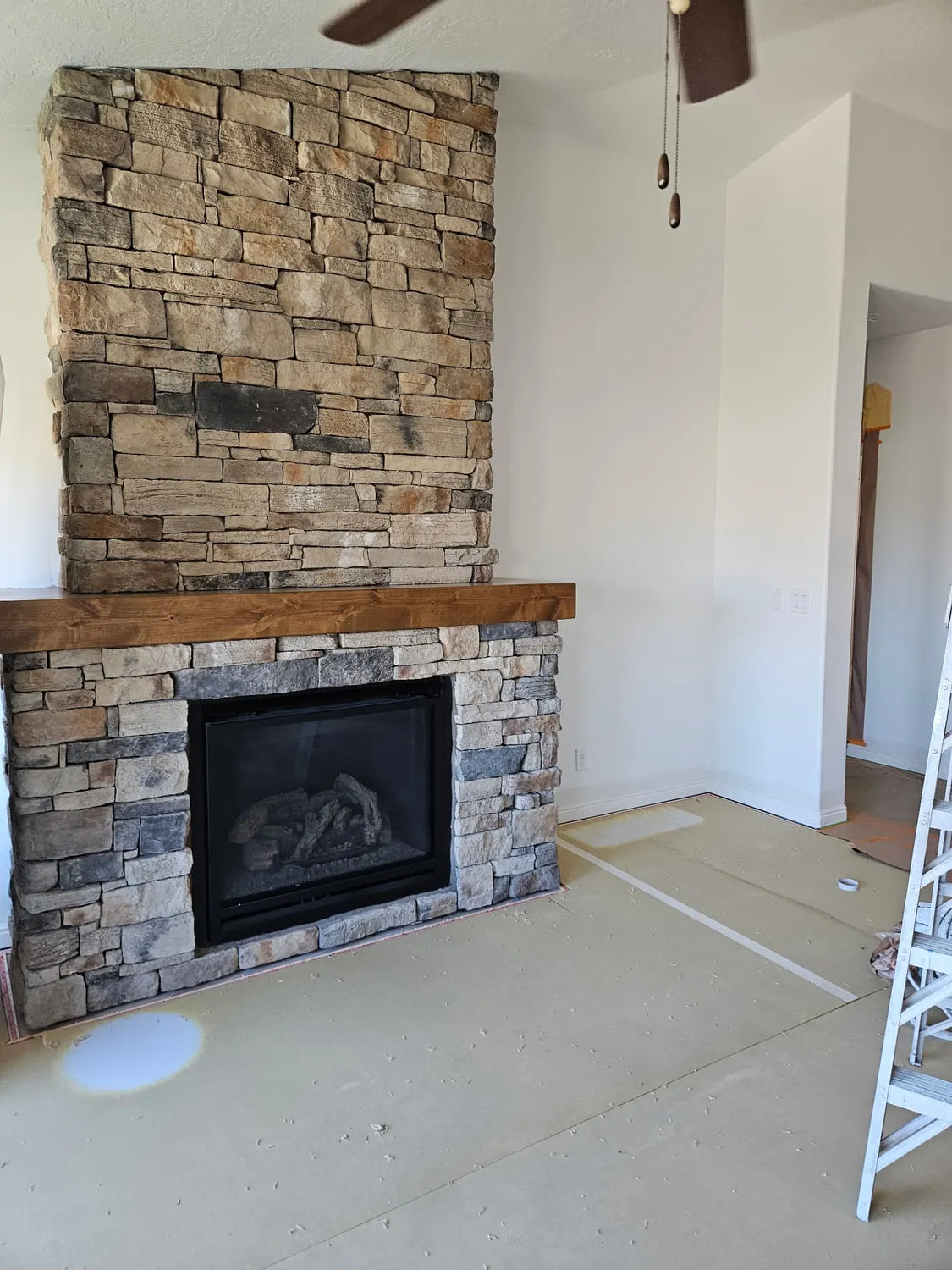 A floor-to-ceiling stacked stone fireplace with a chunky stained timber mantel beam and a gas insert