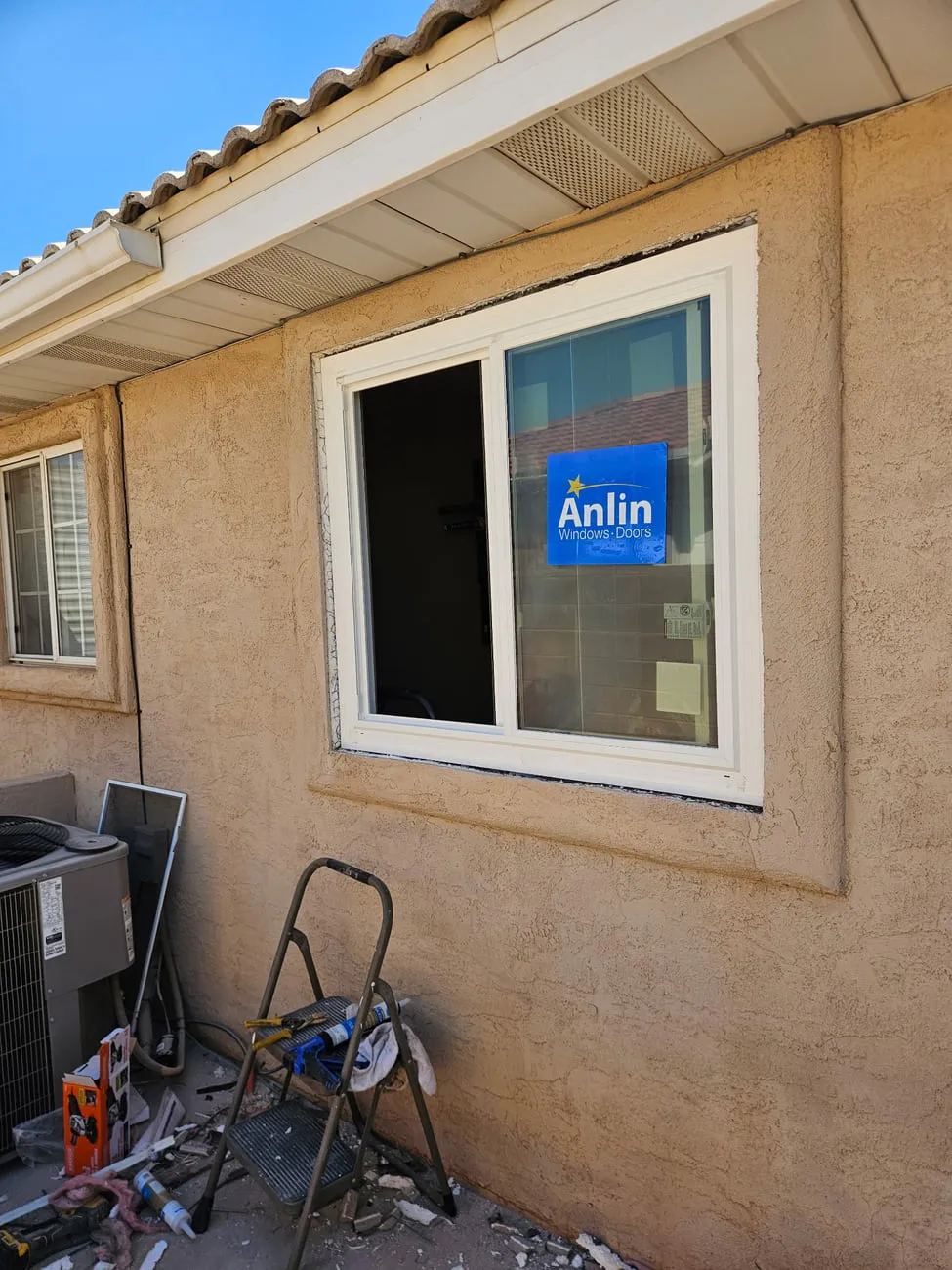 The new vinyl slider seen wider under a tile roof eave with fresh stucco patched around the frame beside an air conditioning condenser