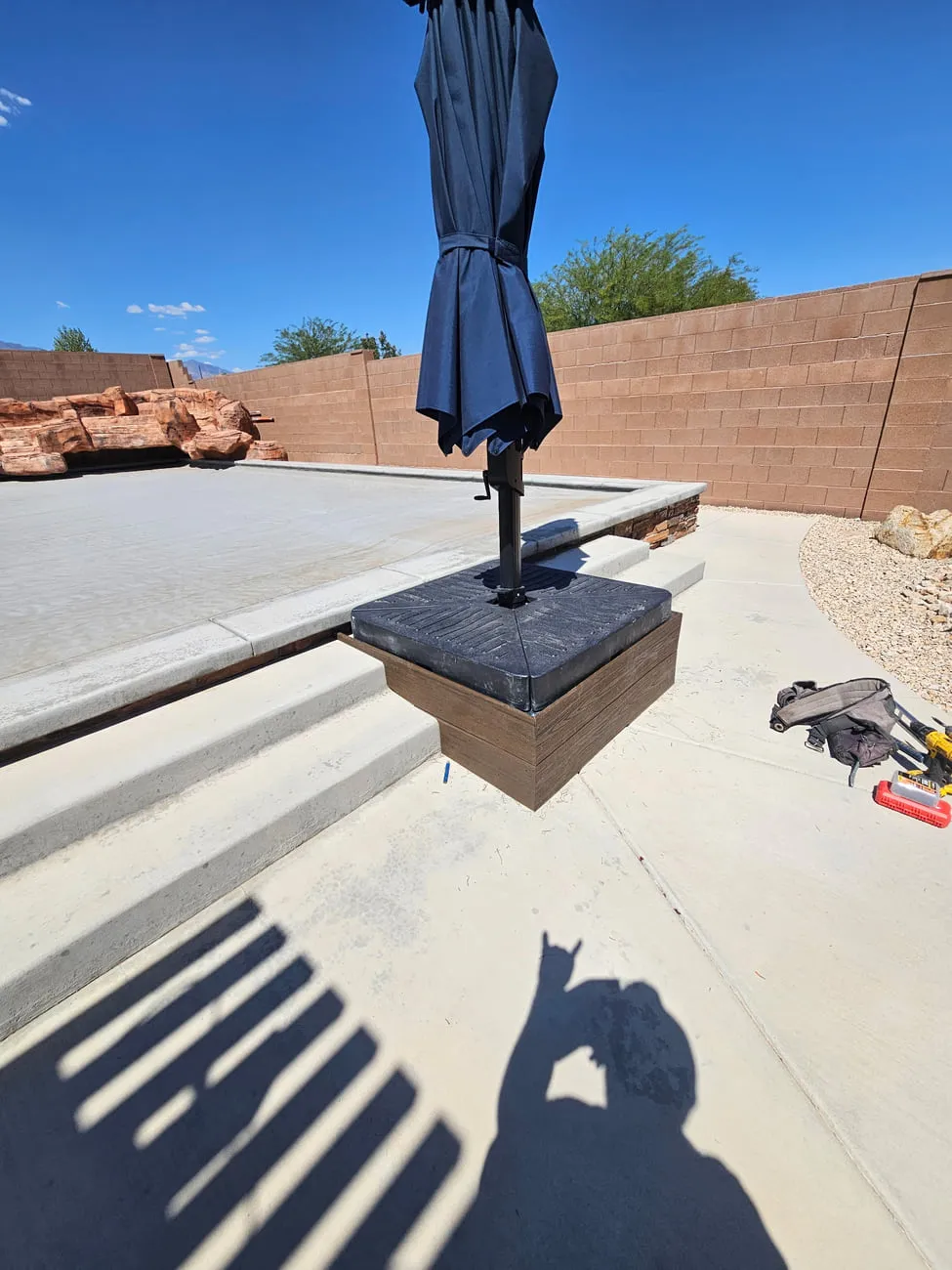 A finished concrete patio and steps with a completed wood-clad cantilever umbrella base on a stone-faced raised slab