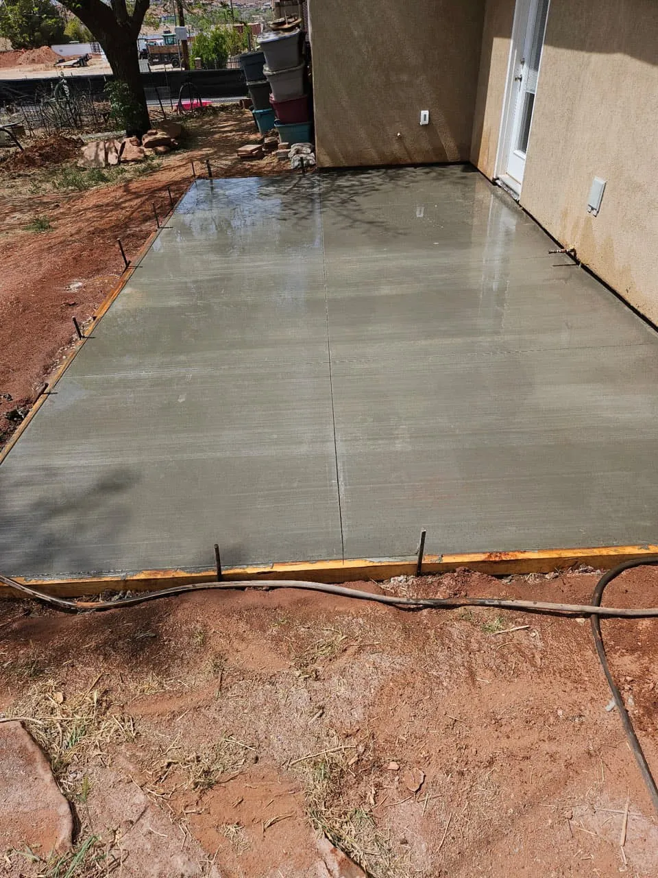 A freshly steel-troweled concrete patio slab against a tan stucco house with wood forms and stakes still in place