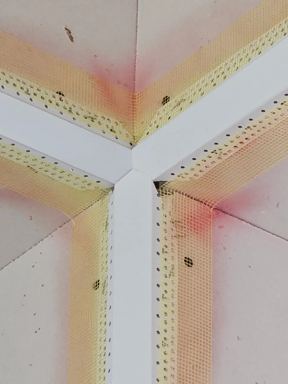 Close view of a three-way drywall corner with paper-faced metal corner bead and a first coat of joint compound