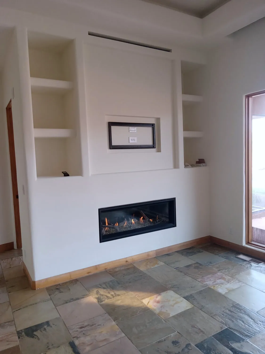 A smooth plaster fireplace wall with radius-corner built-in drywall niches beside a lit linear gas fireplace