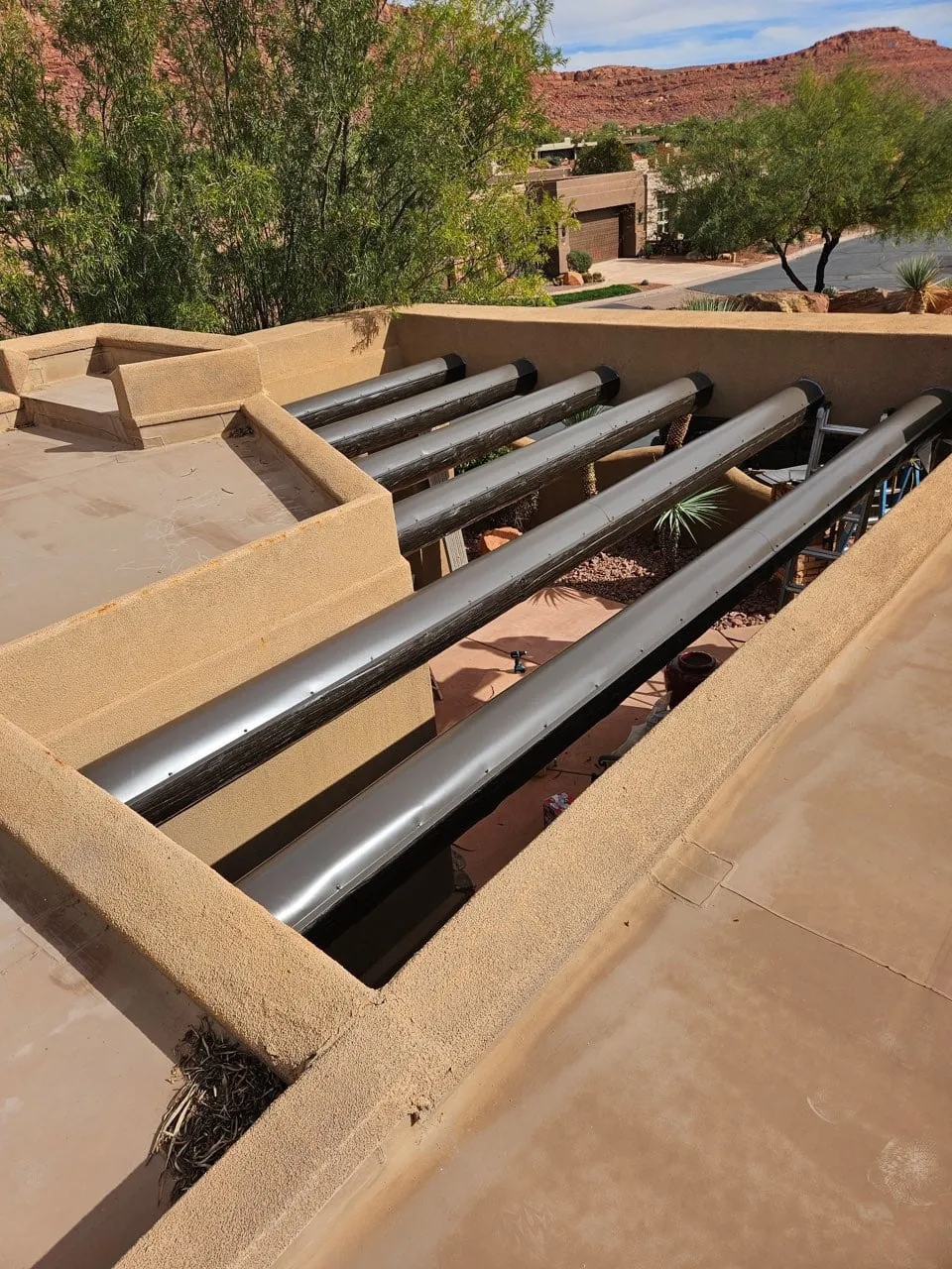 Large round galvanised metal drainage canales staged across a stucco parapet on a flat desert roof with red rock cliffs beyond