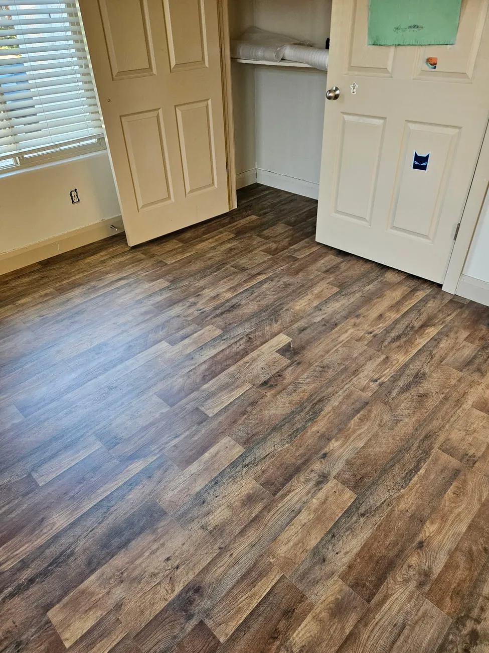 A bedroom with rustic multi-tone brown and grey vinyl plank flooring finished up to cream six-panel doors
