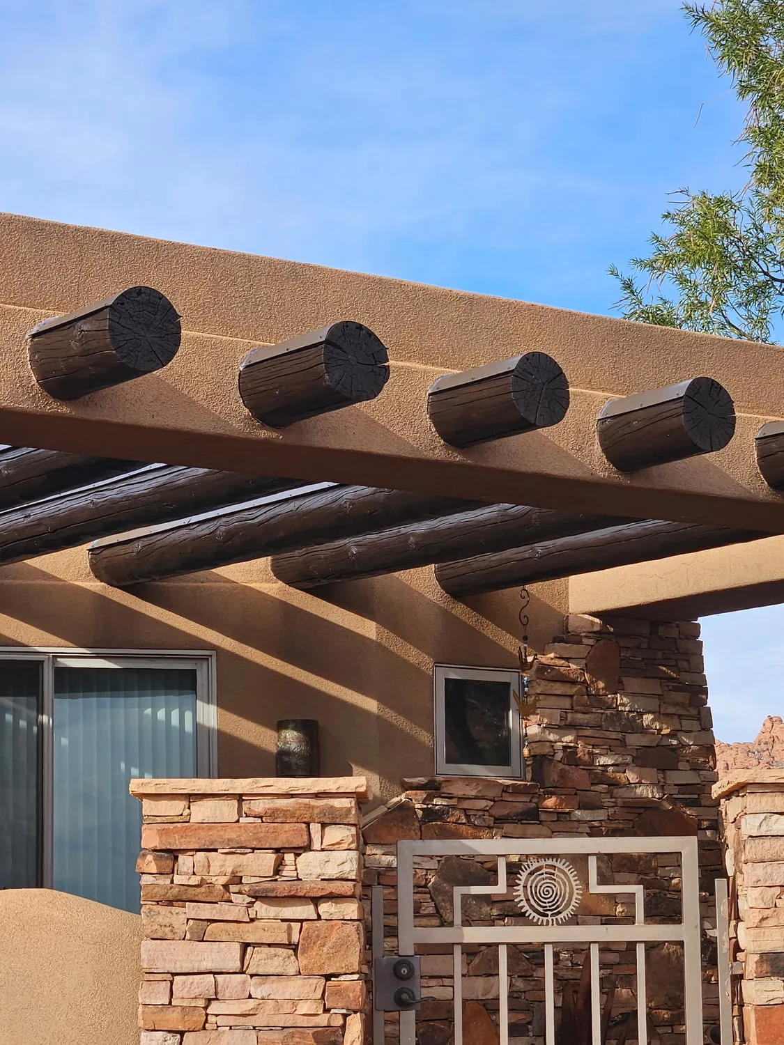 A stucco shade structure with round rustic viga log beams through the header and stacked flagstone columns
