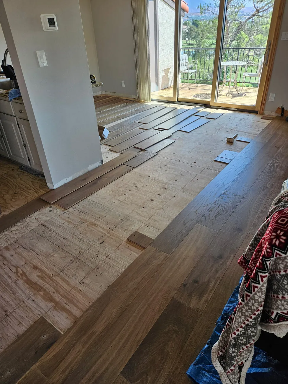 Wide dark engineered plank part-installed over a plywood subfloor with planks racked out ahead of the working row